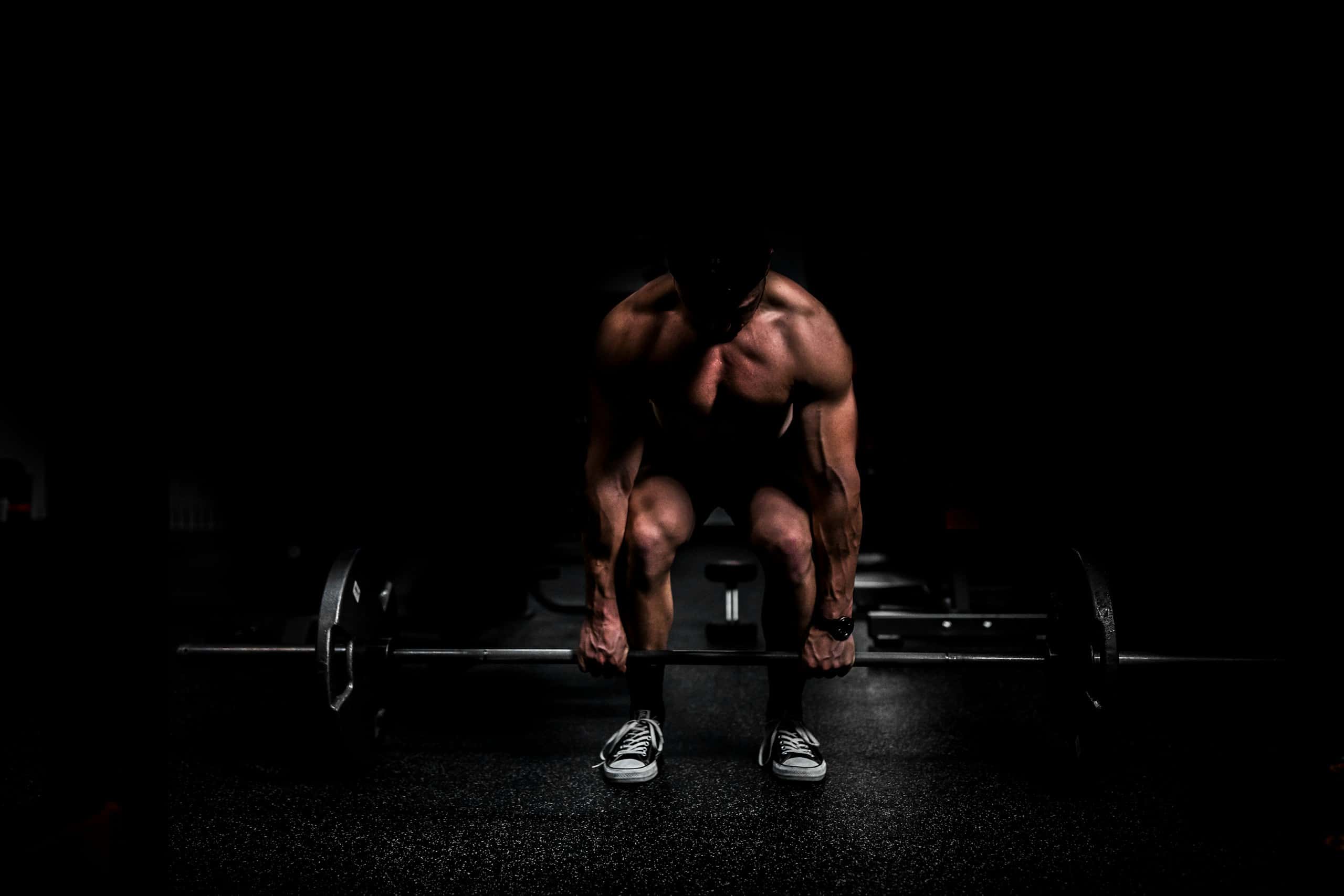 Anonymous athlete in low-key lighting bracing over a loaded barbell before a lift