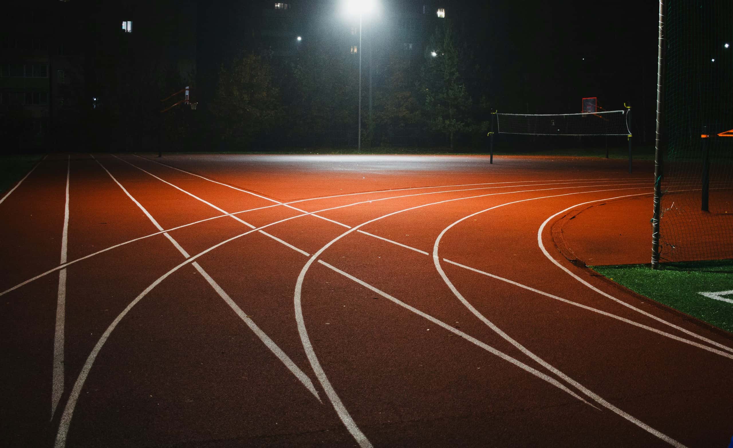 Empty running track at night under a single floodlight, lane lines crisscrossing
