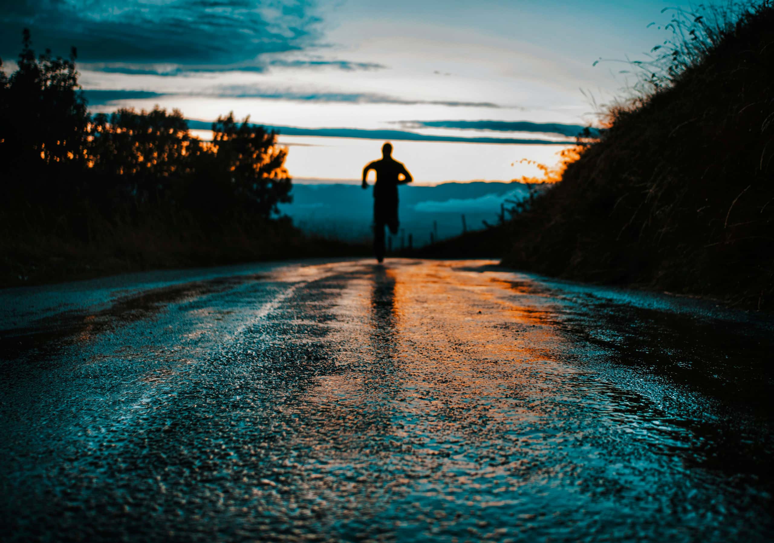 Silhouetted runner approaching down a wet road at dusk